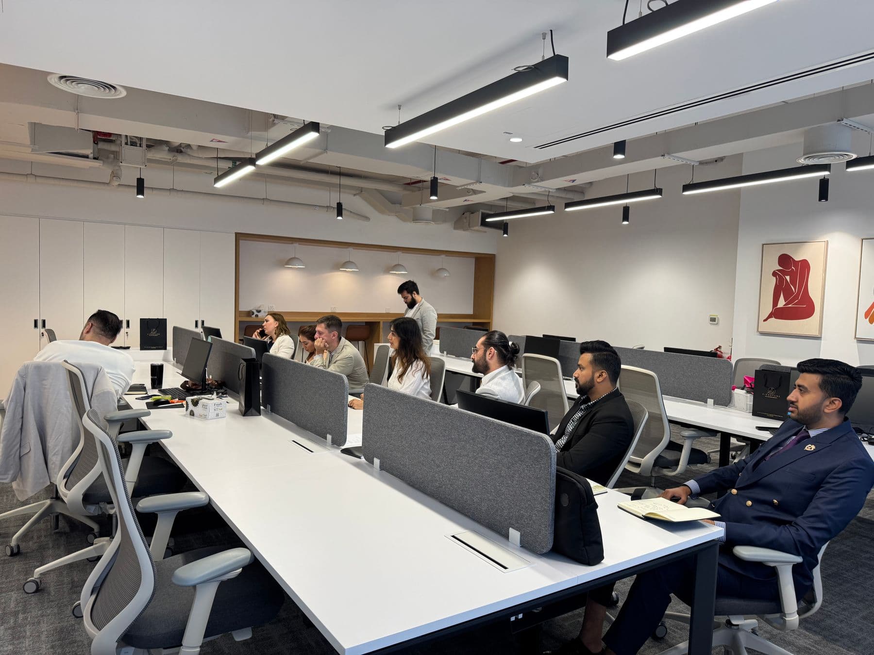 An open-plan office floor with people working at long desks.