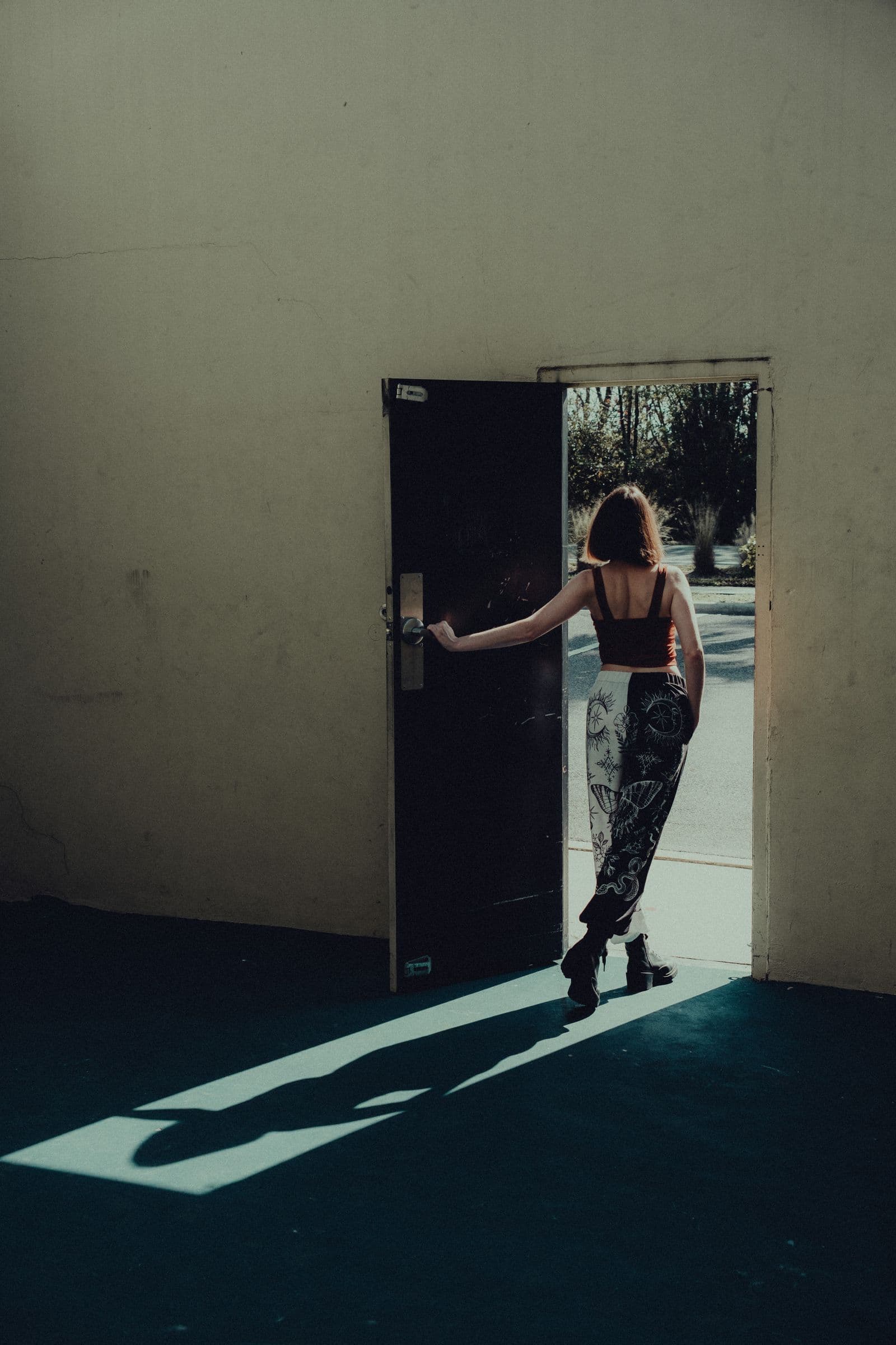 A person seen from behind pushing open a door onto bright daylight.